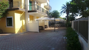 Un patio con mobiliario exterior, una cerca blanca y una palmera.