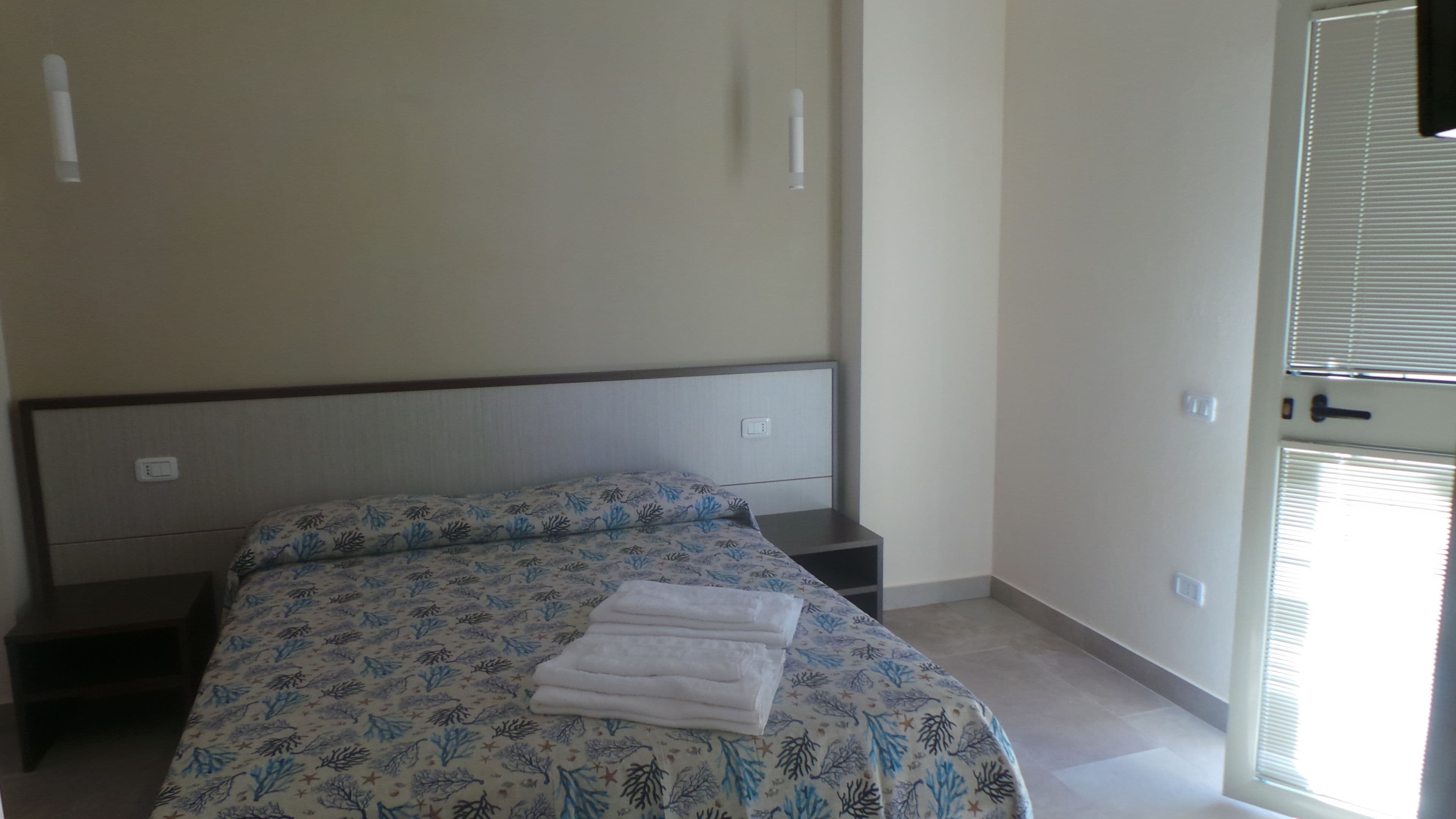 Un dormitorio con cama, mesita de noche, puerta y ventana con persianas.