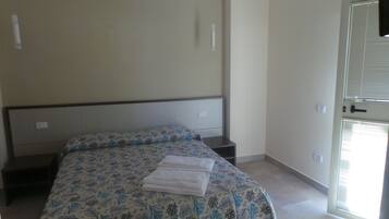Un dormitorio con cama, mesita de noche, puerta y ventana con persianas.