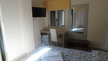 A bedroom with a bed, a desk, a chair, a TV mounted on the wall, and a window.