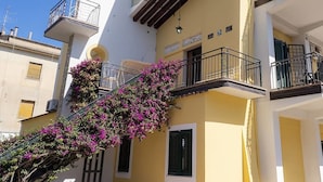 Un edificio de varios pisos con balcones, una escalera adornada con flores rosadas y un cielo azul despejado.