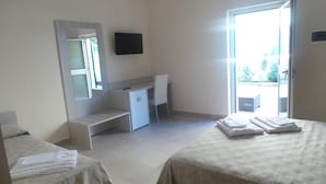 Habitación de hotel con dos camas, un escritorio, una silla, un televisor y una puerta corrediza de vidrio al exterior.