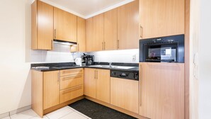 A modern kitchen with wooden cabinets, a black countertop, and a built-in dishwasher. - Pablo II-301 (Koksijde)