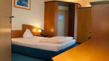 A hotel room with a bed, bedside lamp, and a wooden wardrobe.