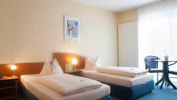 A hotel room with two beds, a small table with a chair, and a painting on the wall.