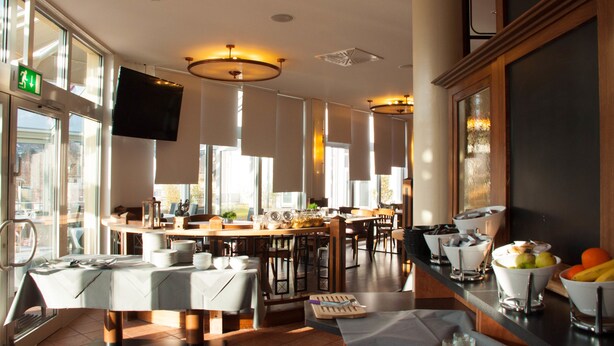 Un espace de restauration moderne dans un hôtel, doté d’un grand buffet pour le petit-déjeuner, de nombreux espaces de repos et d’une grande fenêtre laissant entrer la lumière naturelle.