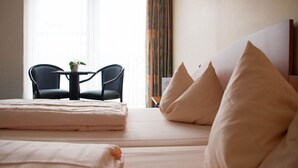 Une chambre d’hôtel avec un lit, deux chaises, une petite table et une fenêtre avec des rideaux.