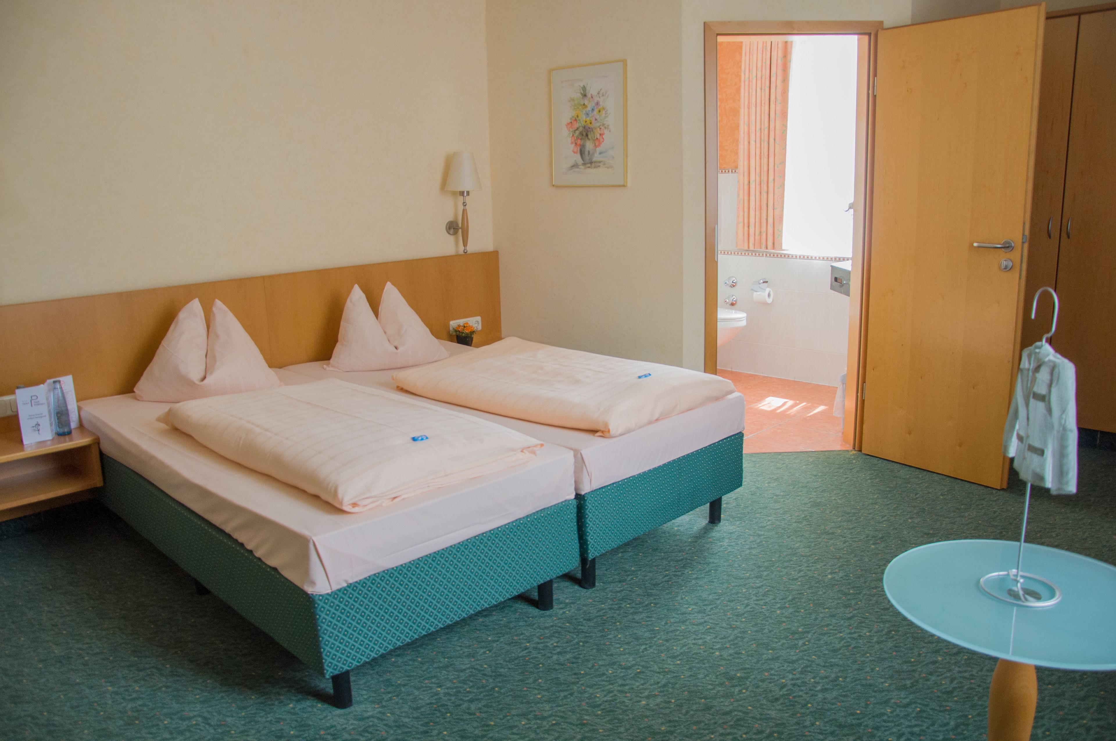 Ein Hotelzimmer mit zwei Betten, einem kleinen Tisch, einer Wandlampe und einer Tür zu einem Badezimmer.