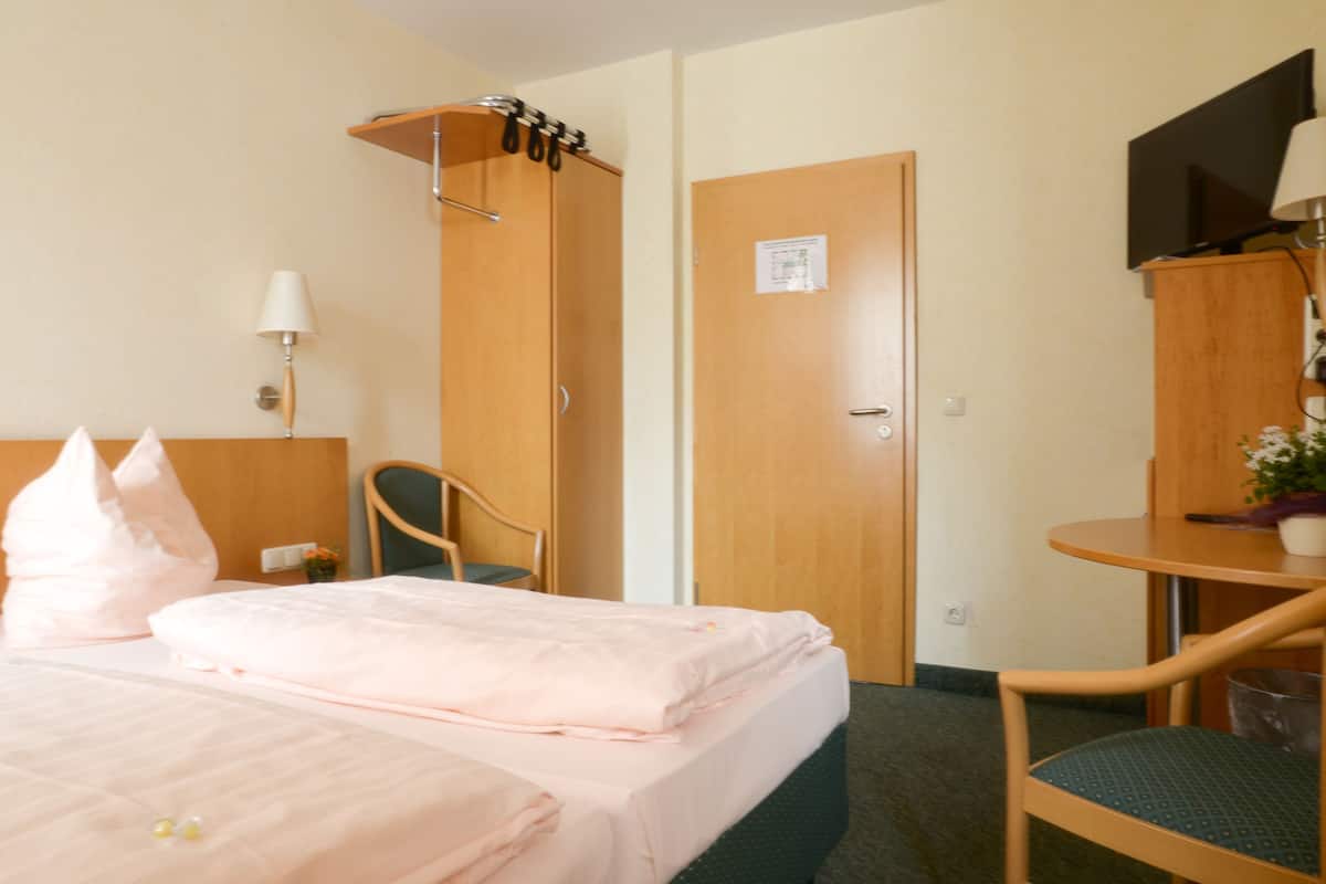 Una habitación de hotel con cama, una silla, escritorio, televisor y puerta.