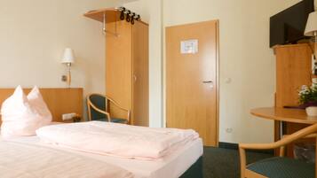 A hotel room with a bed, a chair, a desk, a TV, and a door.