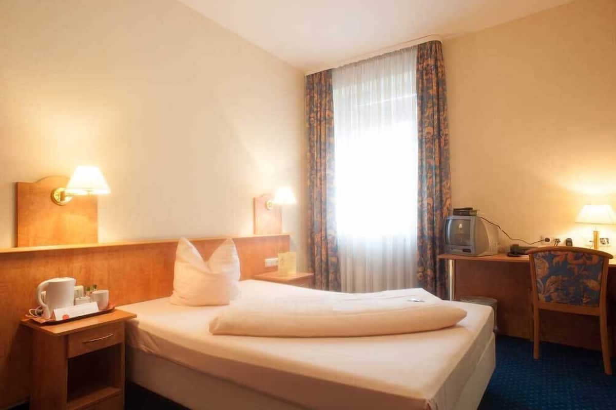 Una habitación de hotel con cama, mesitas de noche, escritorio con televisor y una silla.