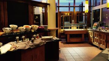 A well-lit breakfast bar with various food items and condiments, wooden cabinets, and a large window offering a view of the sky.