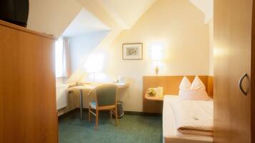 A hotel room with a bed, a desk with a chair, a lamp, and a picture on the wall.