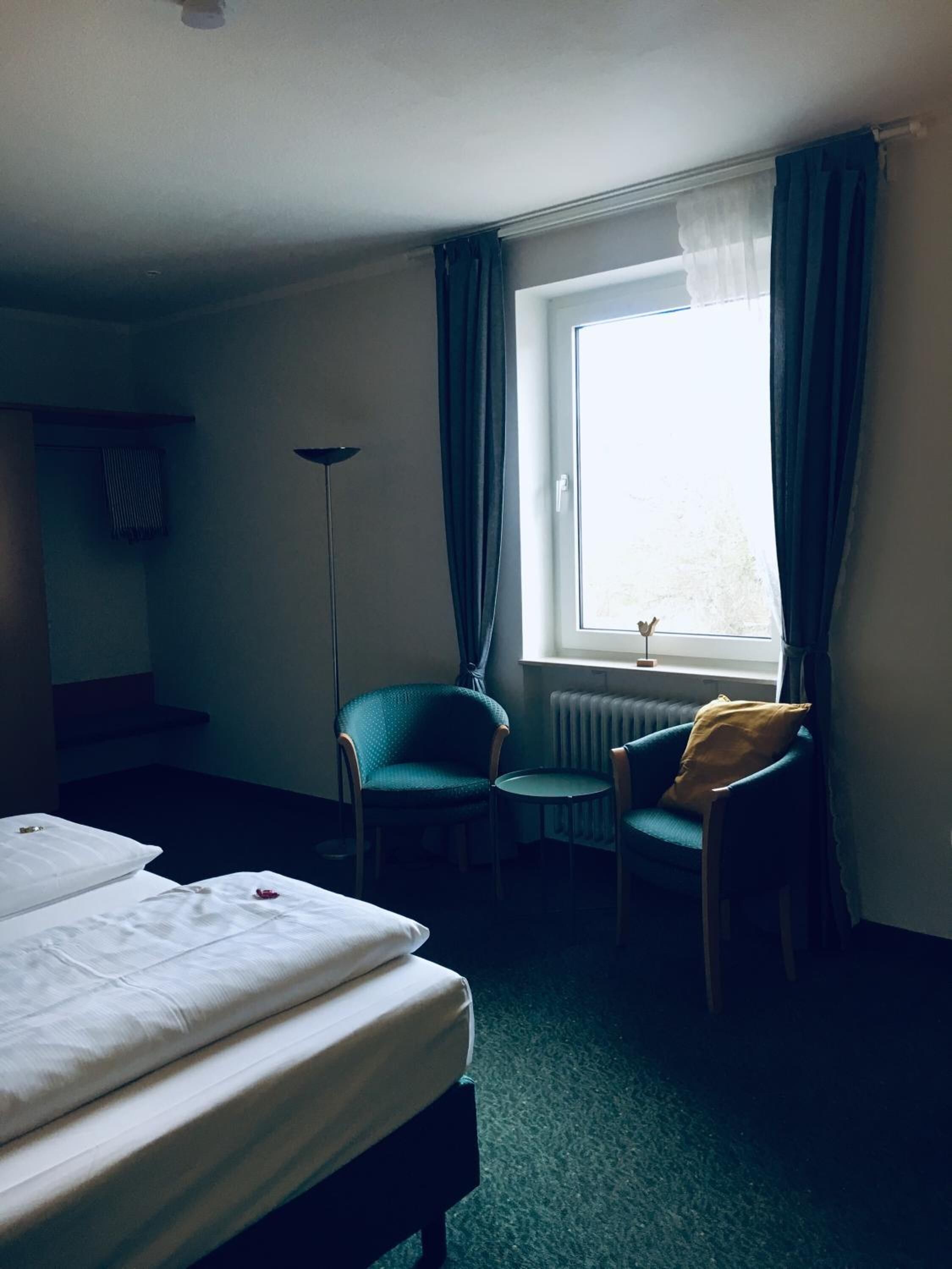 Et hotelværelse med to senge, en stol, et lille bord og et vindue med gardiner.