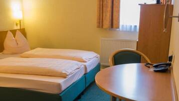 A hotel room with two beds, a desk, a chair, a lamp, and a window with curtains.