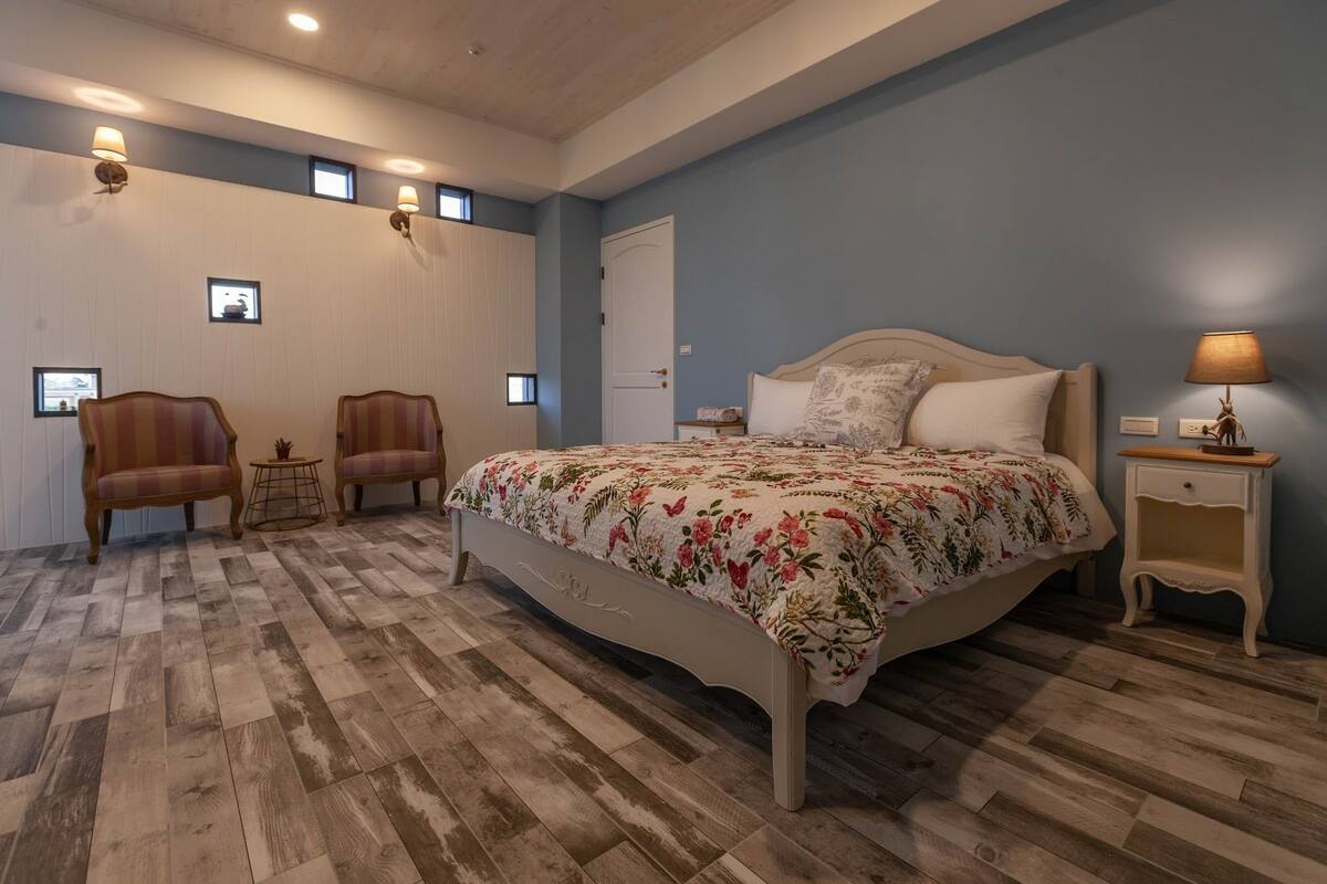 A bedroom with a large bed, two armchairs, a small table, and a nightstand.