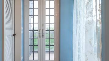 Un pasillo con suelo de madera, una puerta blanca y una ventana con vista a la vegetación.