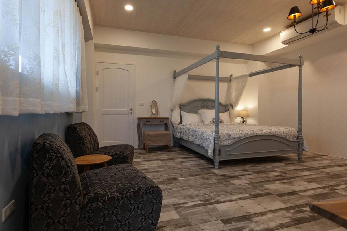 A bedroom with a four-poster bed, a small bedside table, a chair, and a nightstand.