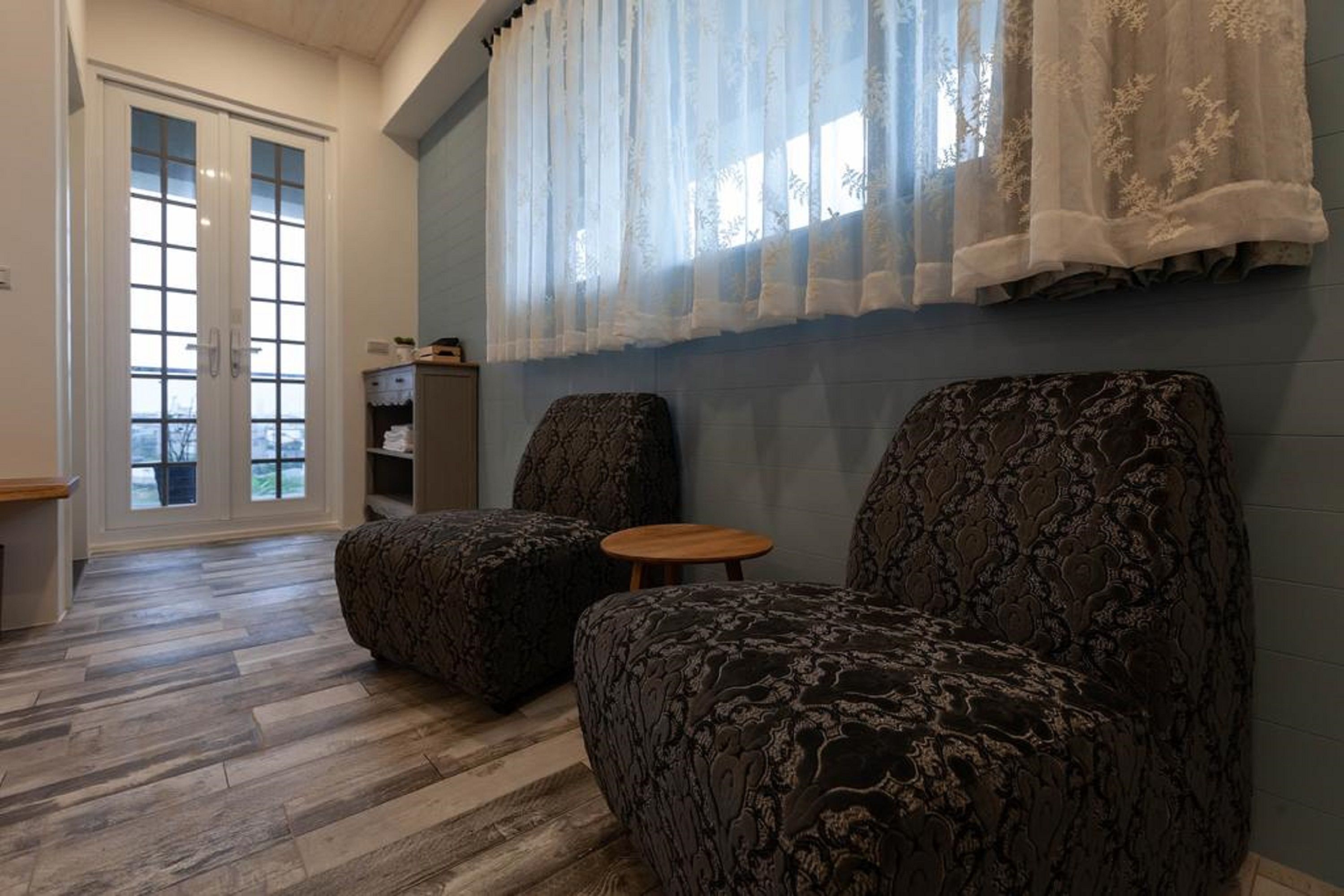 A room with two patterned armchairs, a small wooden table, and a bookshelf.