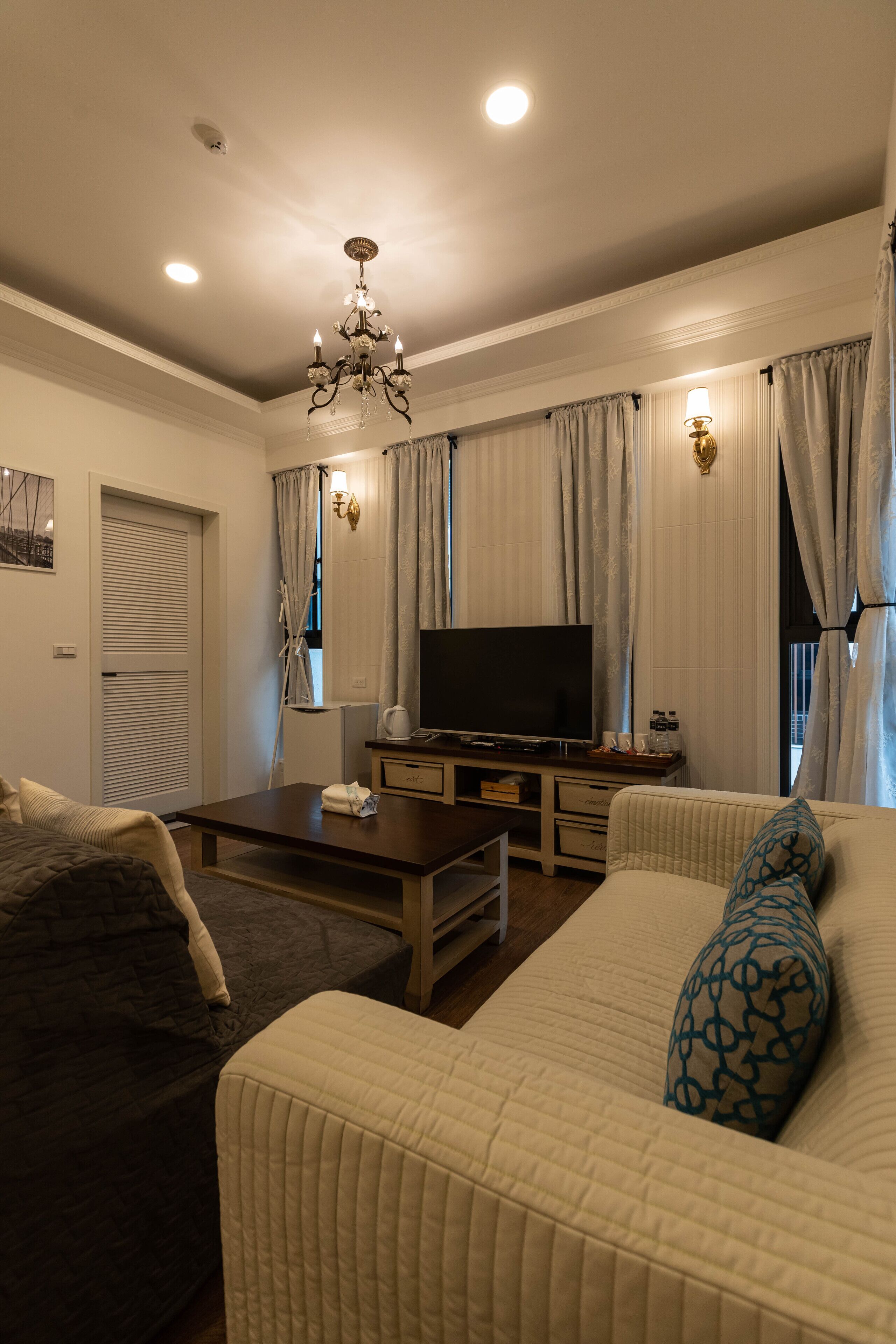 A living room with a sofa, a coffee table, a TV, and a chandelier.