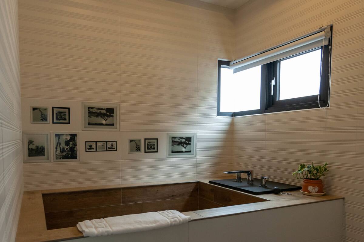 A modern bathroom with a built-in bathtub, a window, and framed pictures on the wall.
