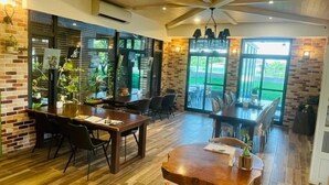 A spacious dining area with wooden tables and chairs, large windows, and a view of the outdoors. - Rambling Snail (Luodong)