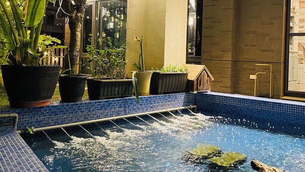 A swimming pool with a tiled edge, surrounded by potted plants and a wooden deck. - Rambling Snail (Luodong)
