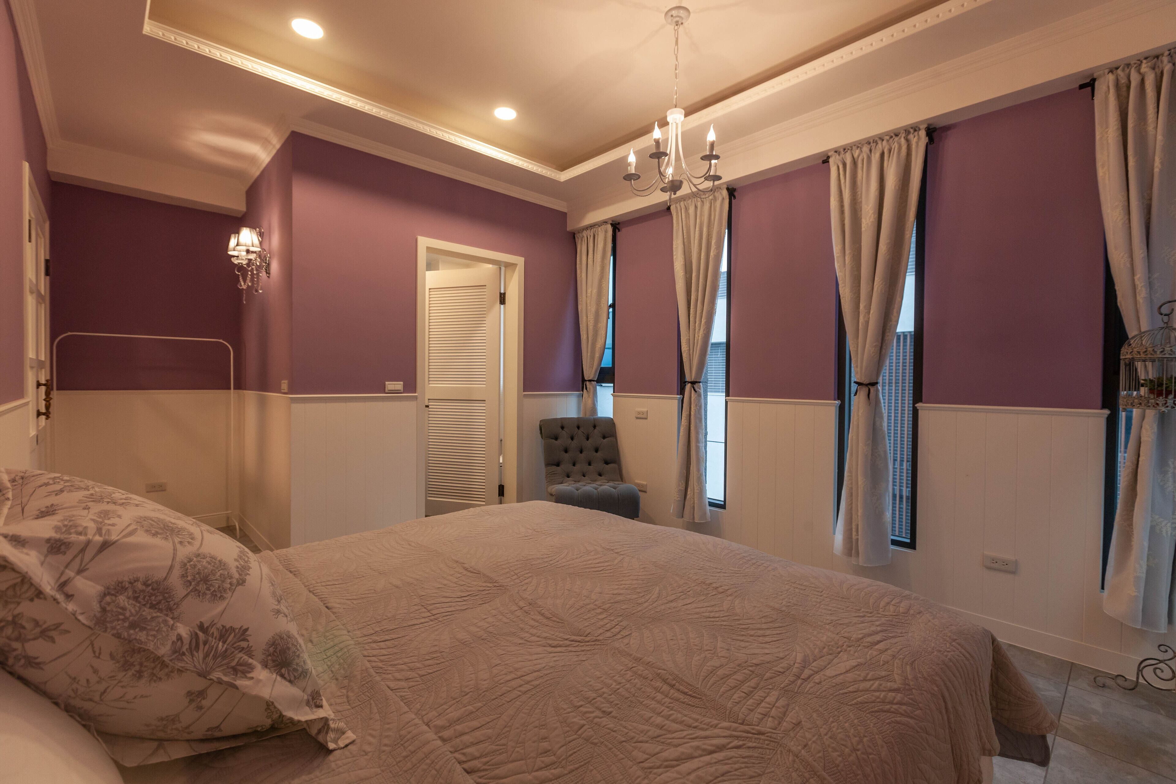 A bedroom with a large bed, a chair, a chandelier, and purple walls.