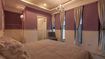 A bedroom with a large bed, a chair, a chandelier, and purple walls.