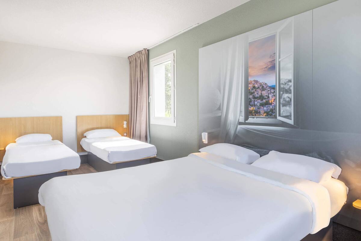 Habitación de hotel con tres camas, un ventanal amplio con vista a un paisaje urbano y una cortina.