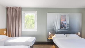 Habitación de hotel con dos camas, una ventana, un cuadro y una mesita de noche con lámpara.