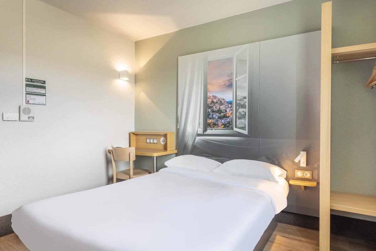 Una habitación de hotel con cama, una silla, una mesita de noche con lámpara y aire acondicionado instalado en la pared.