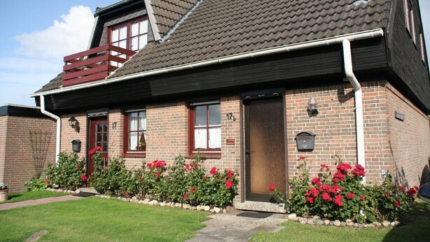 A two-story brick house with a red door, numbered 17, and a small garden with red flowers.