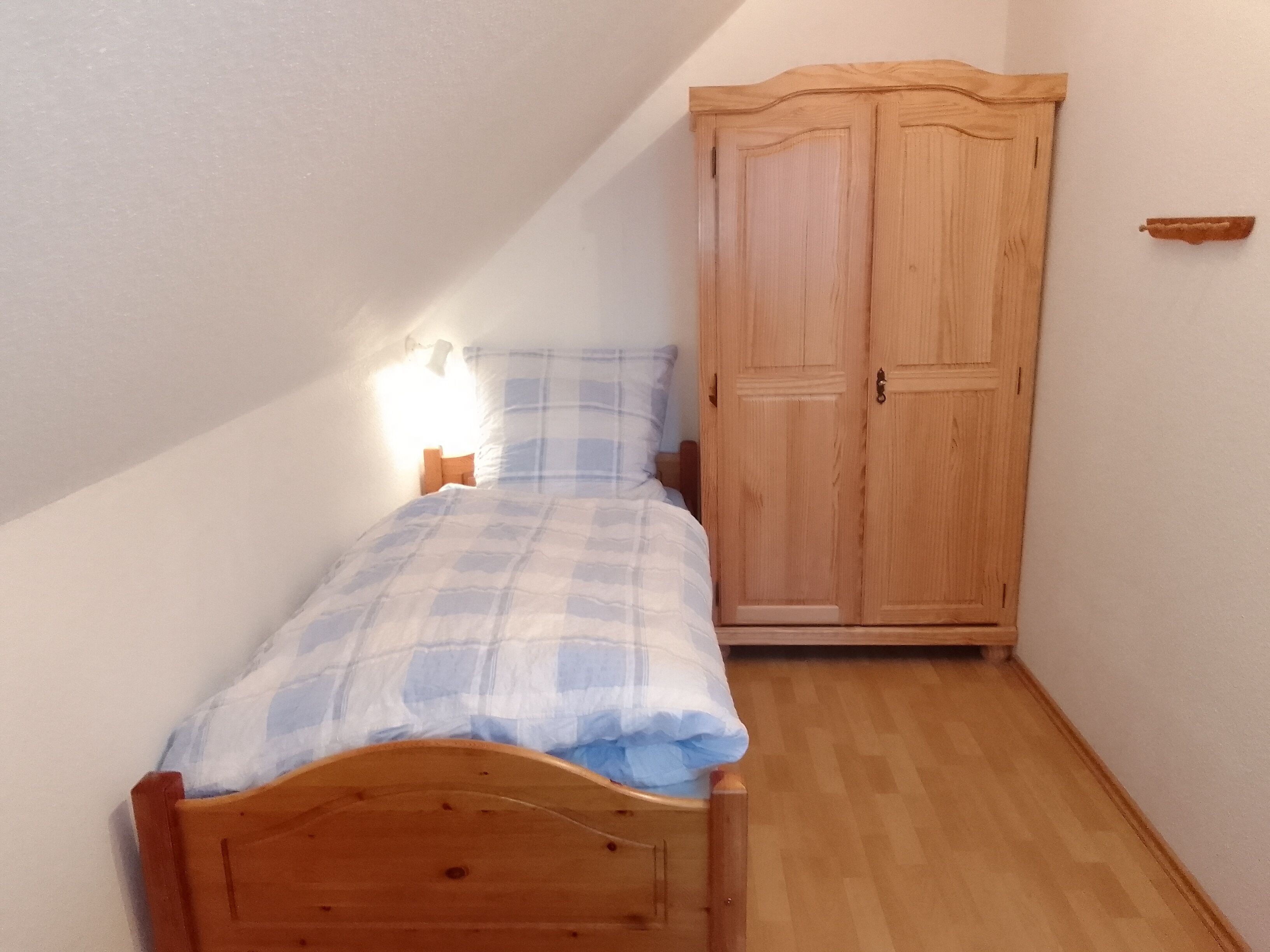 A small, single-bed room with a wooden wardrobe and a bedside table.