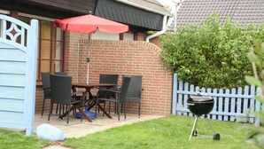 A patio with a table and chairs, a barbecue grill, and a blue fence.