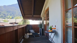 Une terrasse en bois avec un fauteuil de relaxation, une table avec des fruits et des verres, et une vue sur une montagne boisée.