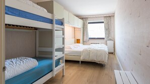 Dormitorio con literas, una cama individual, un escritorio y una ventana con cortinas.