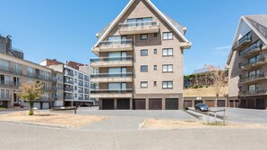 Un edificio residencial de varios pisos con balcones, zona de estacionamiento y cielo despejado.