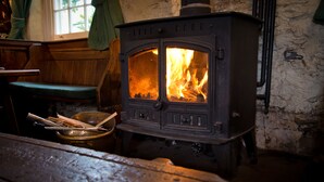 A traditional wood-burning stove with visible flames, a wooden bench, and a rustic interior. - Monsal Head Hotel (Buxton)