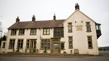 A two-story building with a sign reading "Mansal Head Hotel." It features a traditional architectural style with a pitched roof, multiple windows, and a prominent entrance with a door and a small porch area.