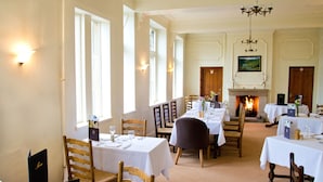 A dining area with multiple tables set for service, a fireplace, and a chandelier. - Monsal Head Hotel (Buxton)