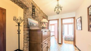 Un pasillo con pared de ladrillo, perchero, cómoda y candelabro.
