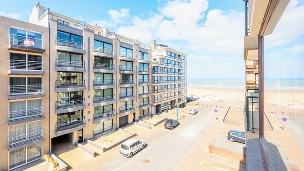 Un edificio residencial de varios pisos con balcones, un estacionamiento y vistas a la playa.