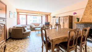Un área de comedor con una mesa y sillas de madera, un sofá y un televisor al fondo.