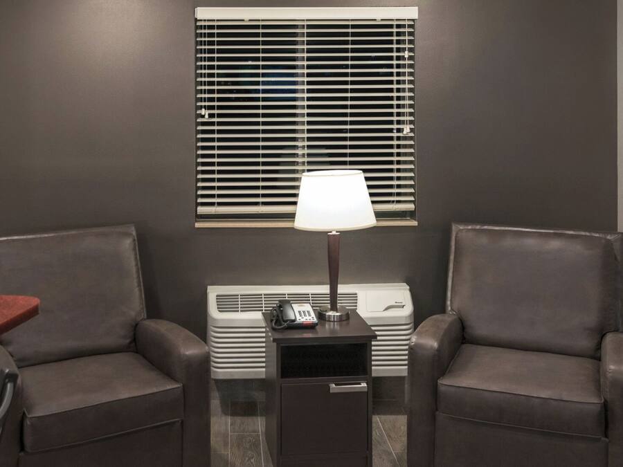 A room with two leather chairs, a small table with a lamp, a heater, and a window with blinds.