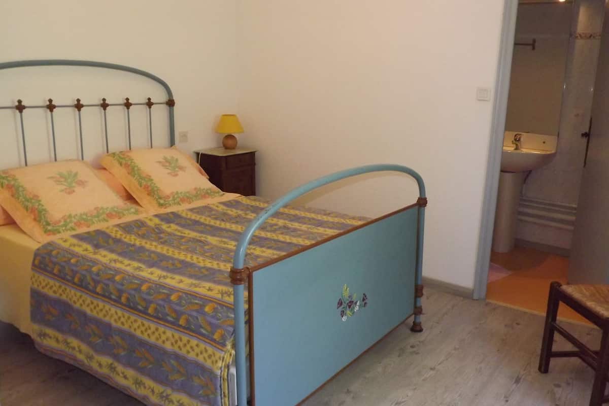 A bedroom with a bed, a chair, a nightstand, and a bathroom visible through an open door.