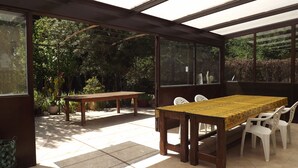 A sunlit patio with a wooden table and chairs, surrounded by glass walls and potted plants. - La Bastide B&B (Cavaillon)