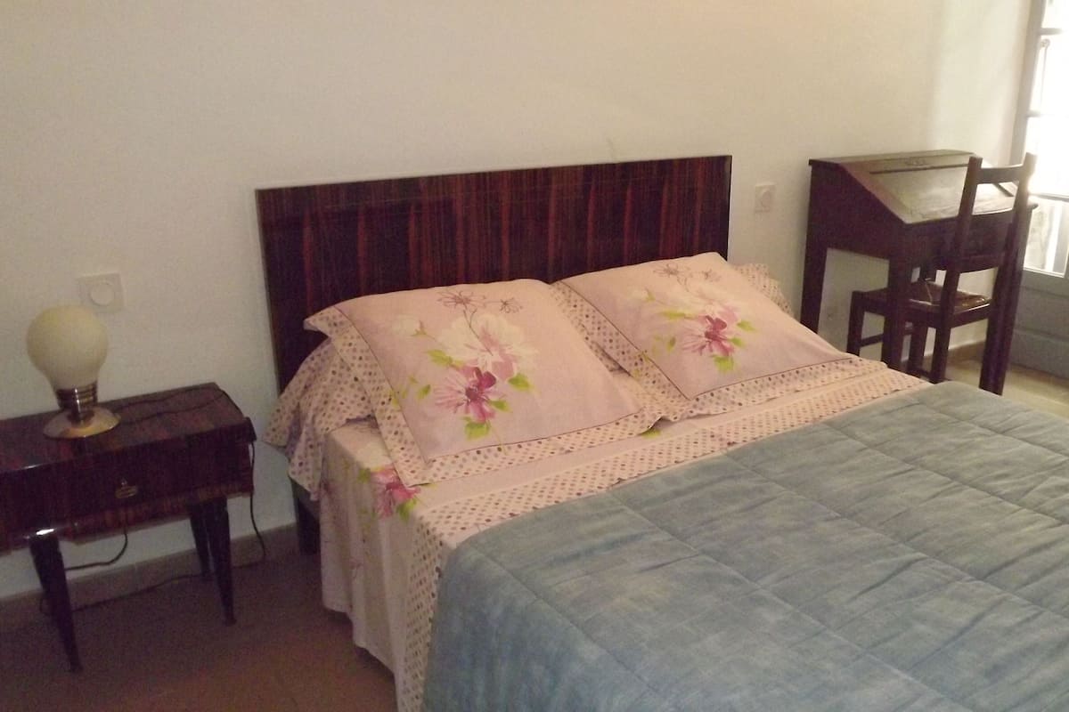 A bedroom with a bed, a nightstand, a chair, and a window.