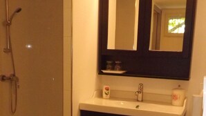 A bathroom with a glass-enclosed shower, a white sink with a dark cabinet, and a mirror above the sink. - La Bastide B&B (Cavaillon)