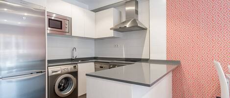A modern kitchen with stainless steel appliances, a built-in washing machine, and a patterned wall.